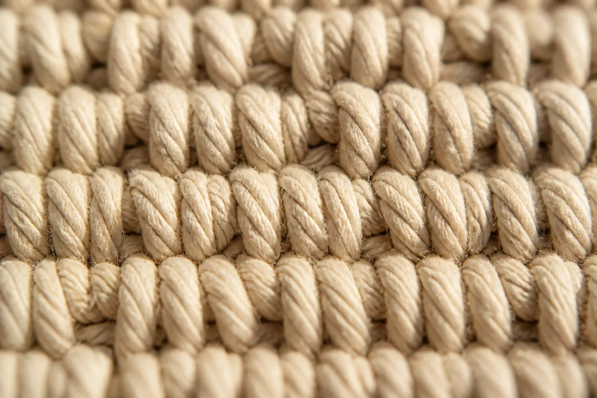 Détail macro d&rsquo;une bande de nœuds plats serrés en coton beige, lumière rasante révélant le relief